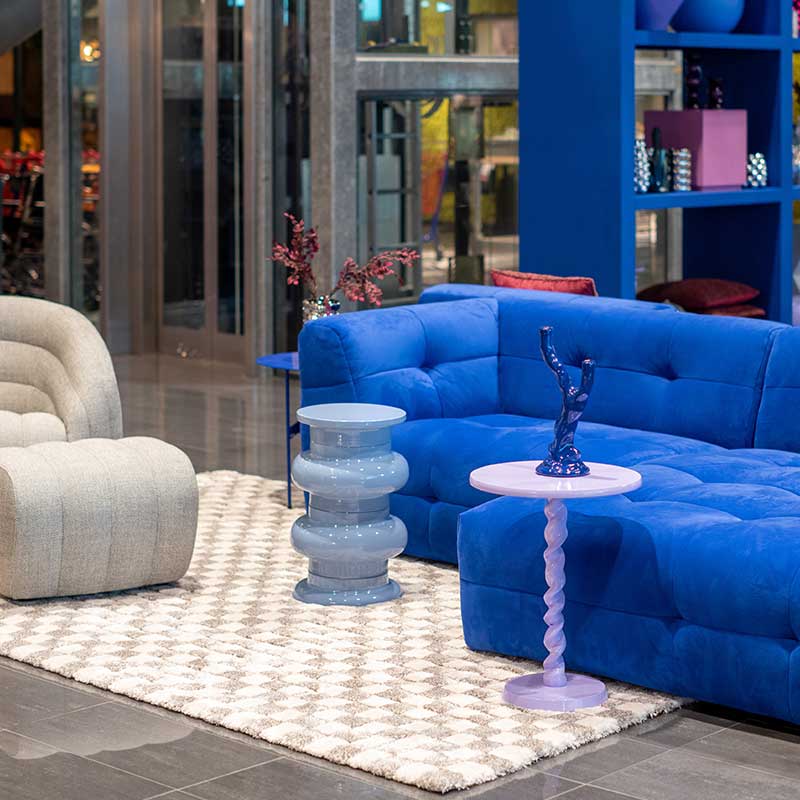 Stijlvolle zithoek met blauwe bank, grijze fauteuil en bijzettafels in pasteltinten op een geometrisch vloerkleed.