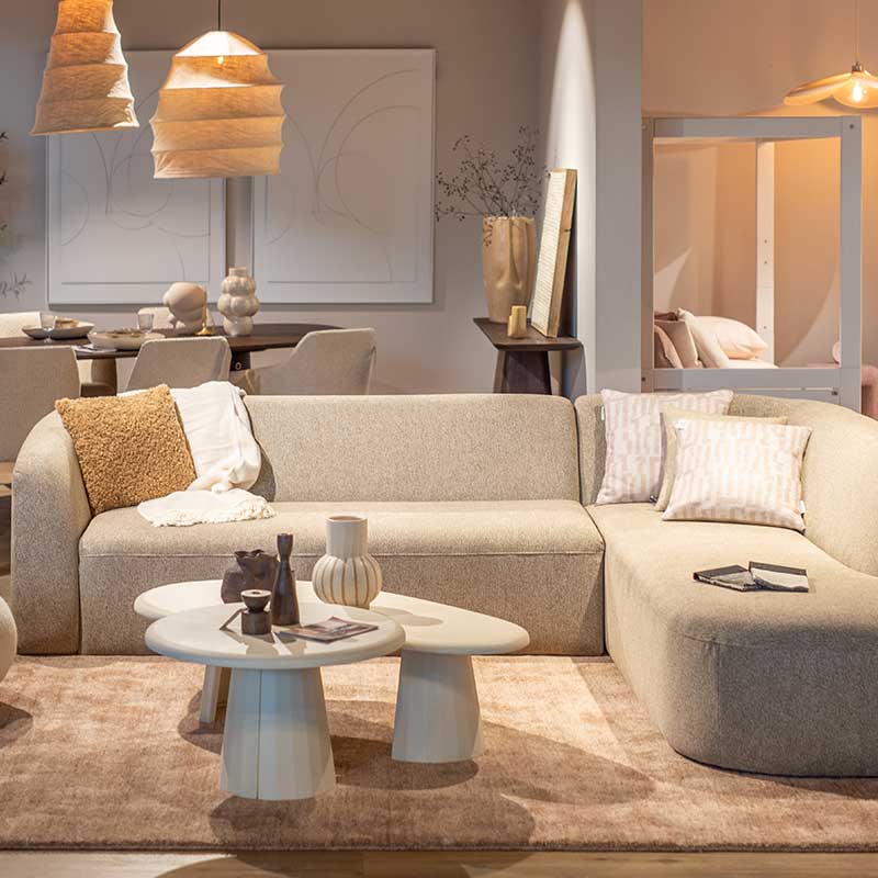 Neutrale woonkamer met lichtgrijze bank, houten tafels en beige decoratieve elementen voor een serene uitstraling. Dit is Slow Life woontrend 2025.